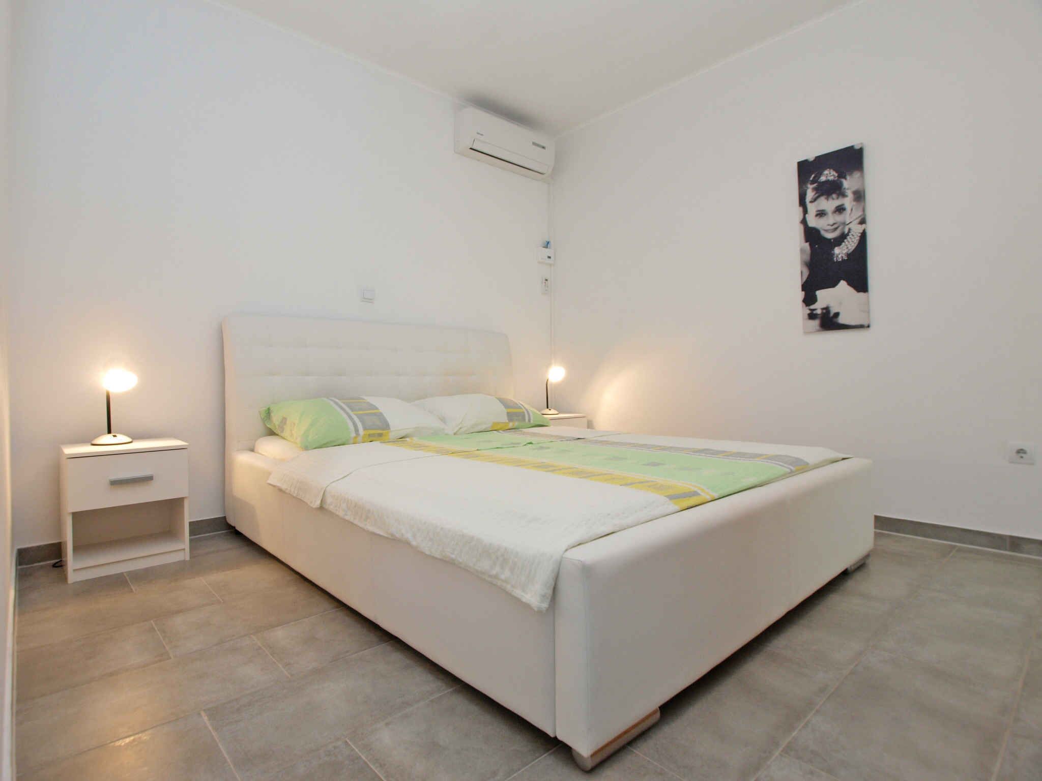 Ein Schlafzimmer mit einem Einzelbett, zwei Nachttischen mit Lampen, einer Wandklimaanlage und einem gerahmten Bild an der Wand.