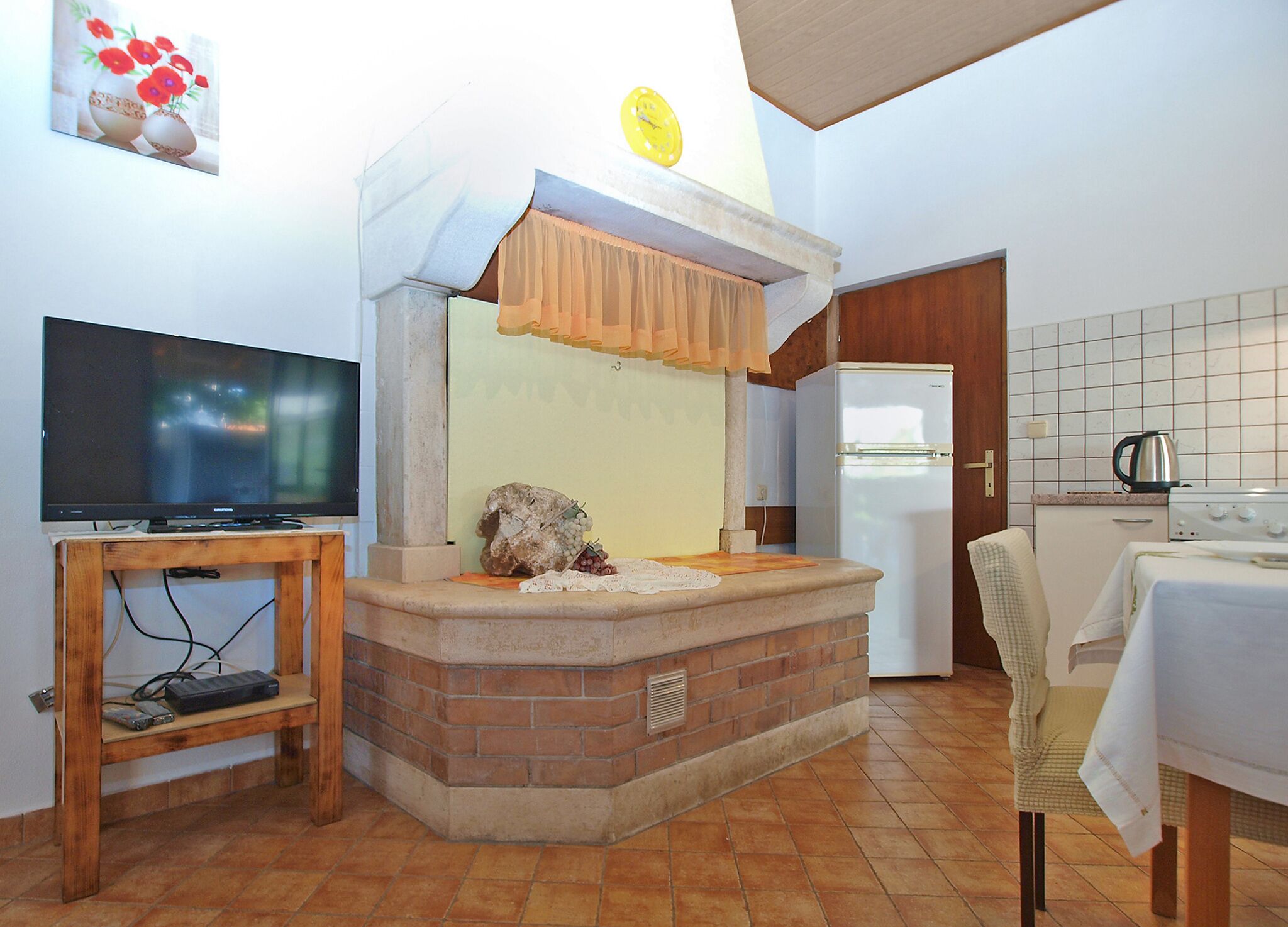 Una cocina compacta con televisor, una pieza central de piedra y un refrigerador.
