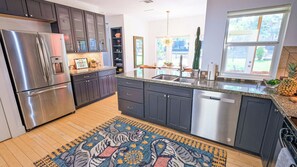 Una cocina moderna con armarios oscuros, electrodomésticos de acero inoxidable, una encimera de granito y una alfombra estampada.