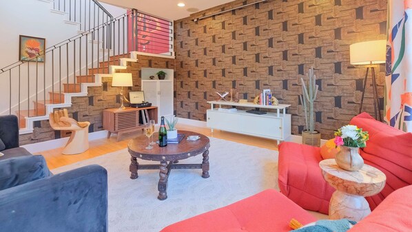 Una sala de estar con escaleras, una pared estampada, una mesa baja con bebidas y un sofá rojo.