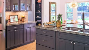 Une cuisine avec des meubles de couleur sombre, un plan de travail en granit et une fenêtre donnant sur un paysage verdoyant.