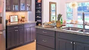 A modern kitchen with dark cabinets, granite countertops, and a built-in wine rack. - Hacienda SoCo - Fire Pit & 3 Min Walk to SoCo (Austin)