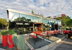 Un restaurante con terraza, fachada de vidrio y letreros que anuncian hamburguesas y papas fritas.
