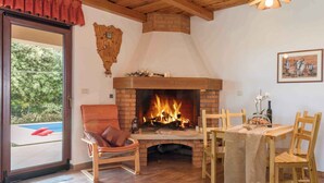 A cozy room with a fireplace, a dining table with chairs, a leather chair, and a view of a swimming pool through a glass door. - Holiday apartment with pool (Ližnjan)