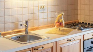 A kitchen with a stainless steel sink, a gas stove, wooden cabinets, and a fruit bowl on the counter. - Holiday apartment with pool (Ližnjan)