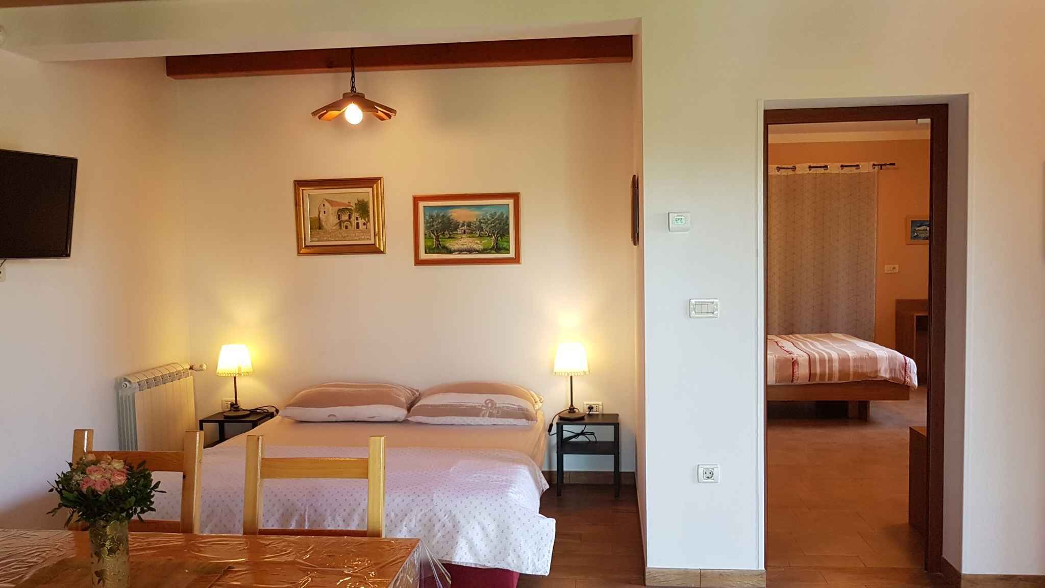 A bedroom with a bed, bedside tables, a lamp, a radiator, and two framed pictures on the wall.