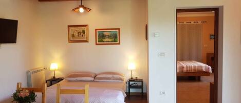 A bedroom with a bed, bedside tables, a lamp, a radiator, and two framed pictures on the wall.