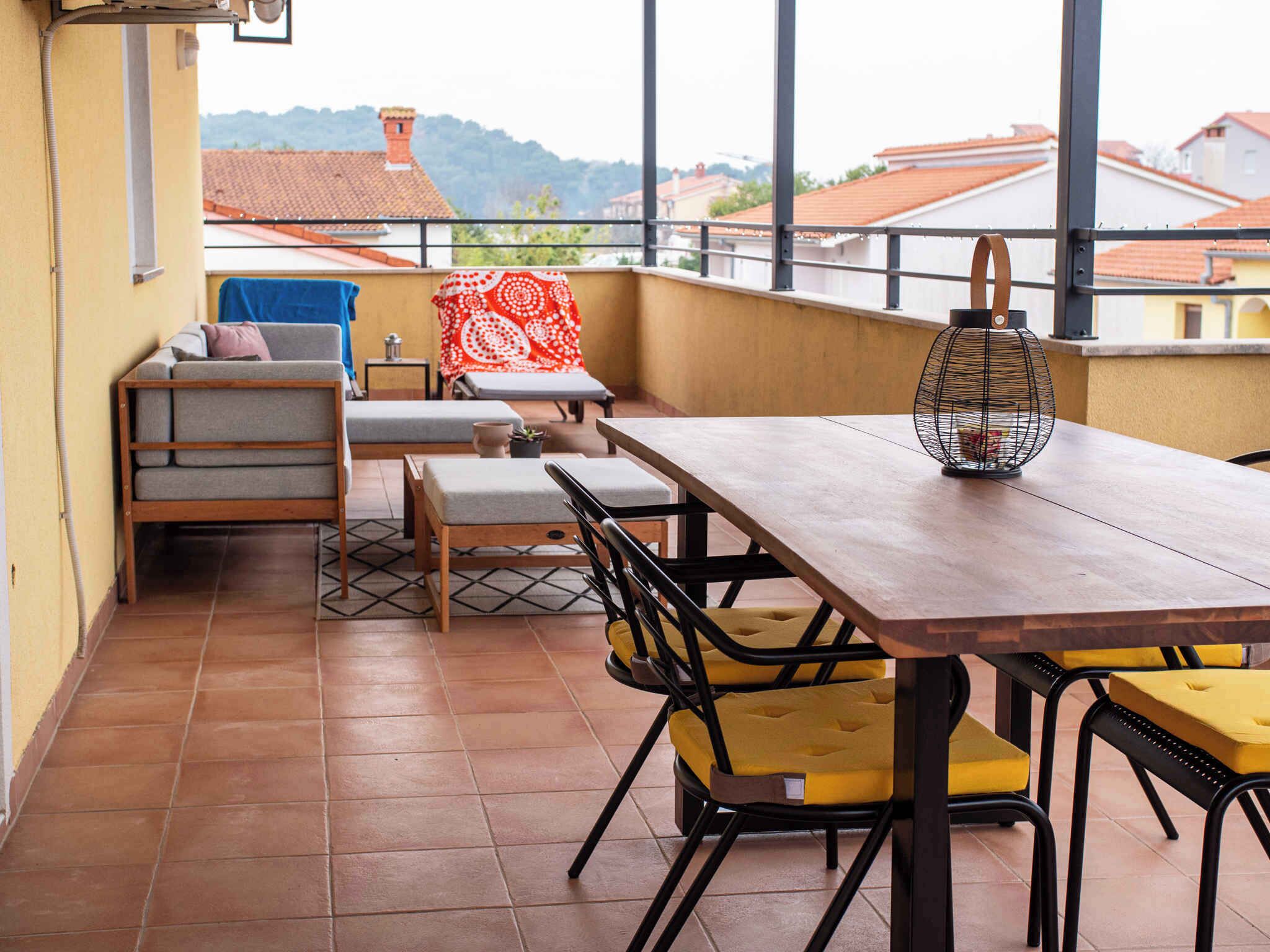 A balcony with a wooden table, yellow chairs, a sofa, and a red patterned tablecloth.