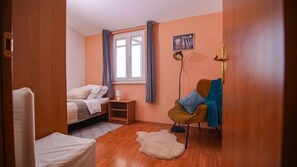 Cozy retreat with a single bed, nightstand, and comfortable chair, set against a soft peach backdrop.
