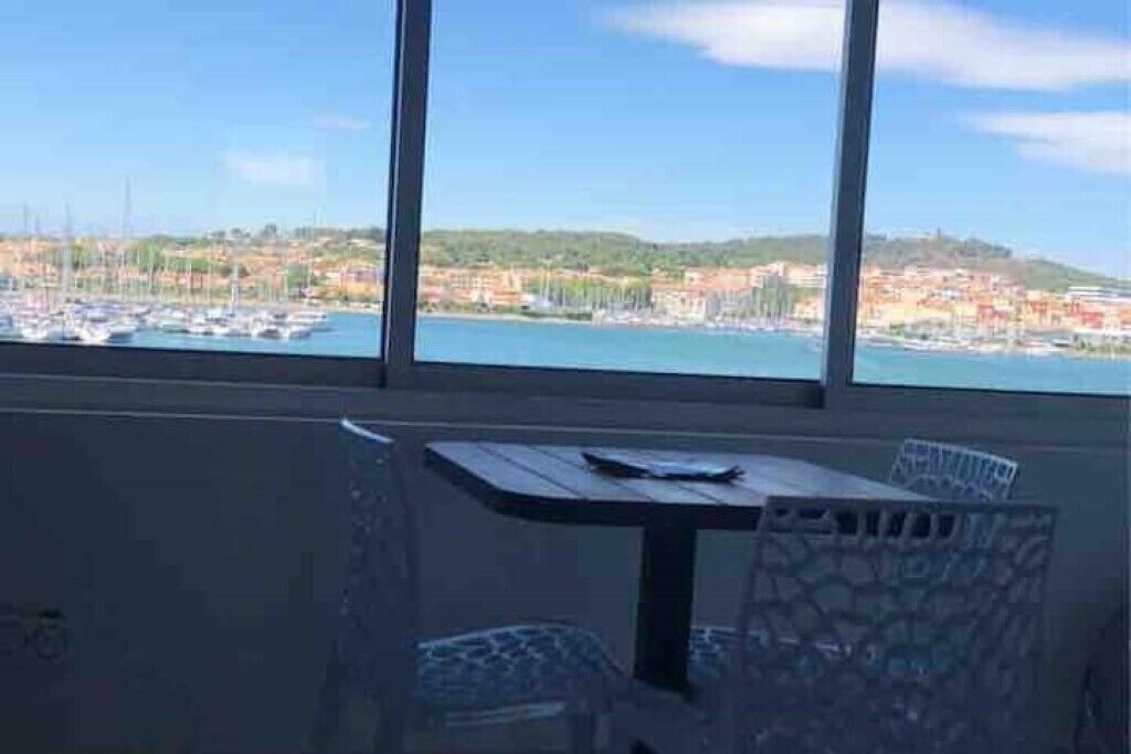 Een kamer met een groot raam, met uitzicht op een jachthaven en een kustplaats.