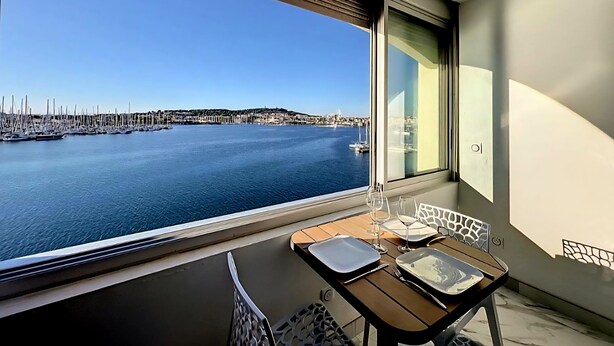 Un balcon avec une table dressée pour le dîner, une vue sur une marina avec des bateaux, et un paysage urbain en arrière-plan.