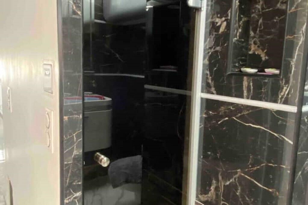 A bathroom with a glass shower enclosure, marble walls, and a towel hanging on the door.