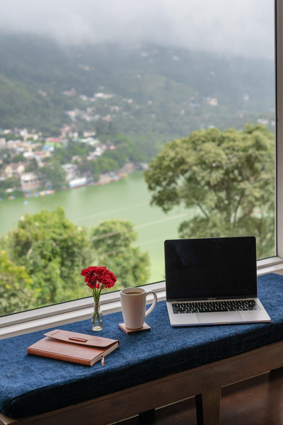 A laptop on a window sill with a view of a green landscape and a river.