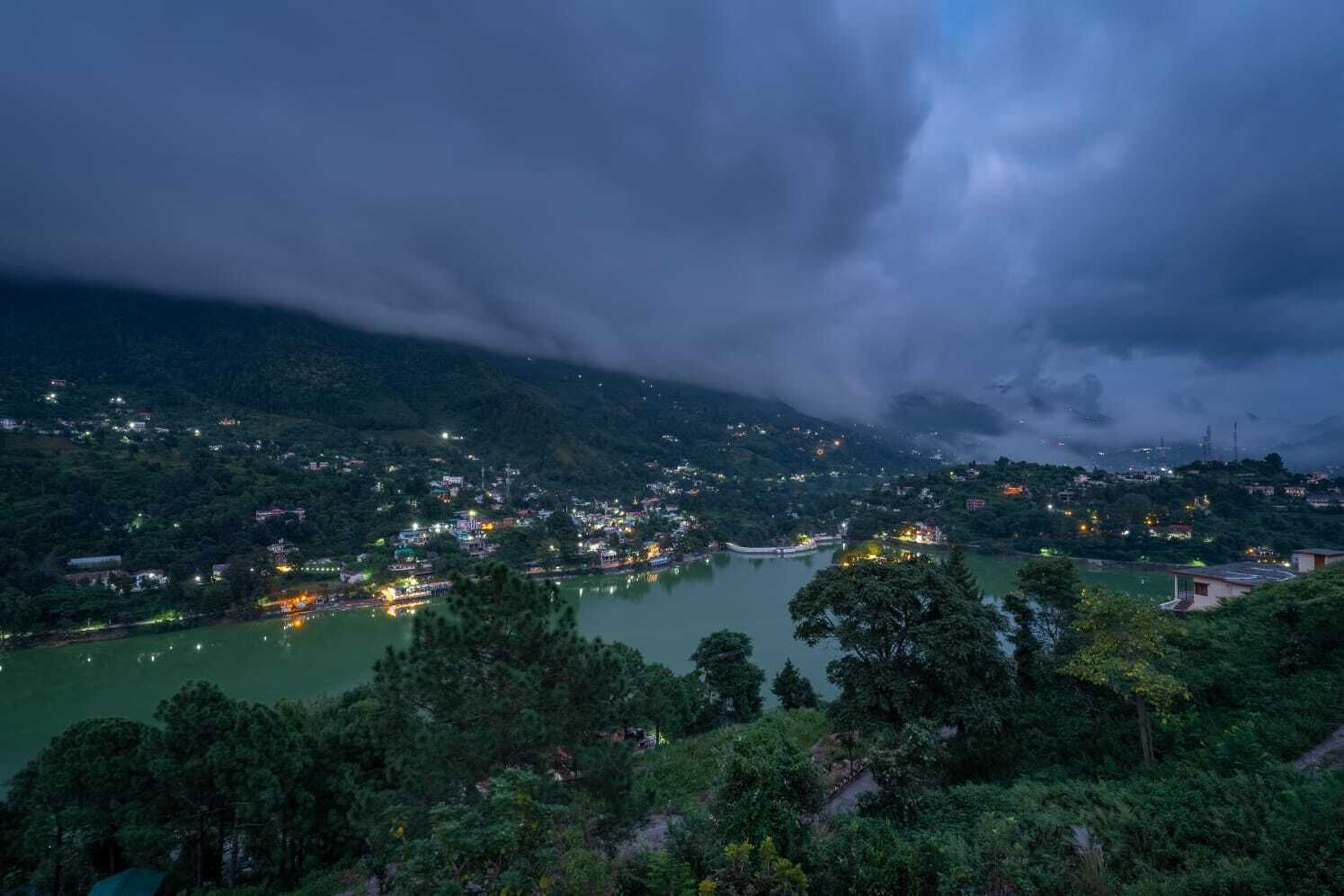 A panoramic view of a town with a river, surrounded by hills and dense greenery.