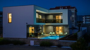 A modern two-story house with a swimming pool, outdoor seating, and a balcony.