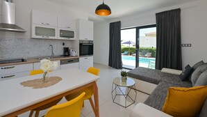 A modern kitchen with white cabinets, a dining table with yellow chairs, and a view of a swimming pool through large windows.