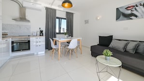 A modern kitchen with white cabinetry, a built-in oven, and a dining area with a table and chairs.