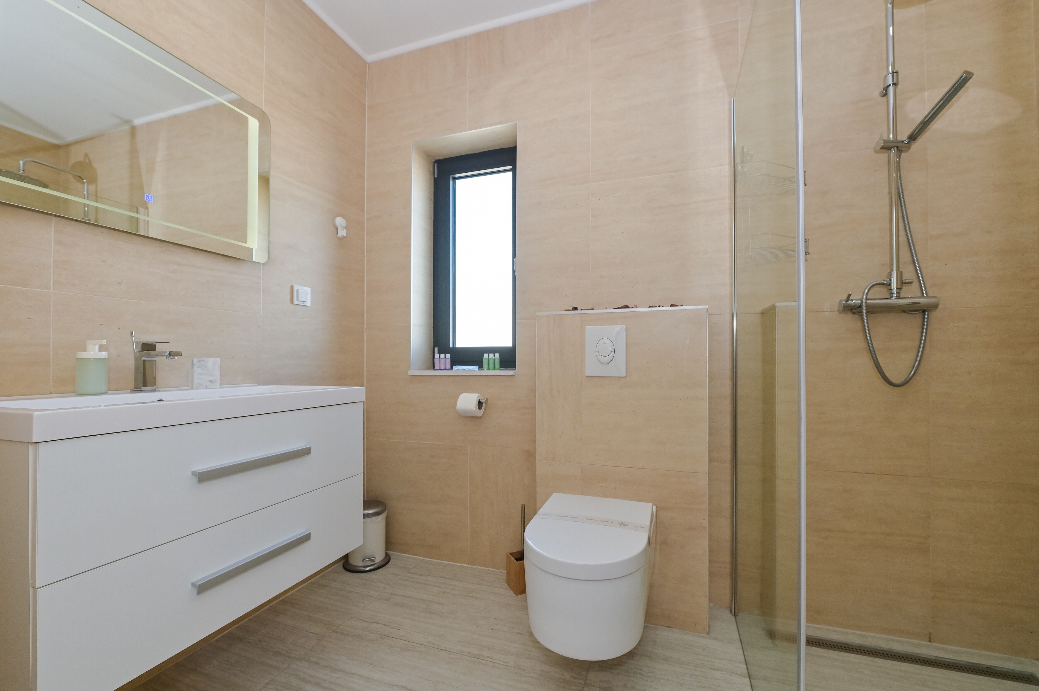 Een moderne badkamer met een witte wastafel, een douchecabine van glas en een klein raam.
