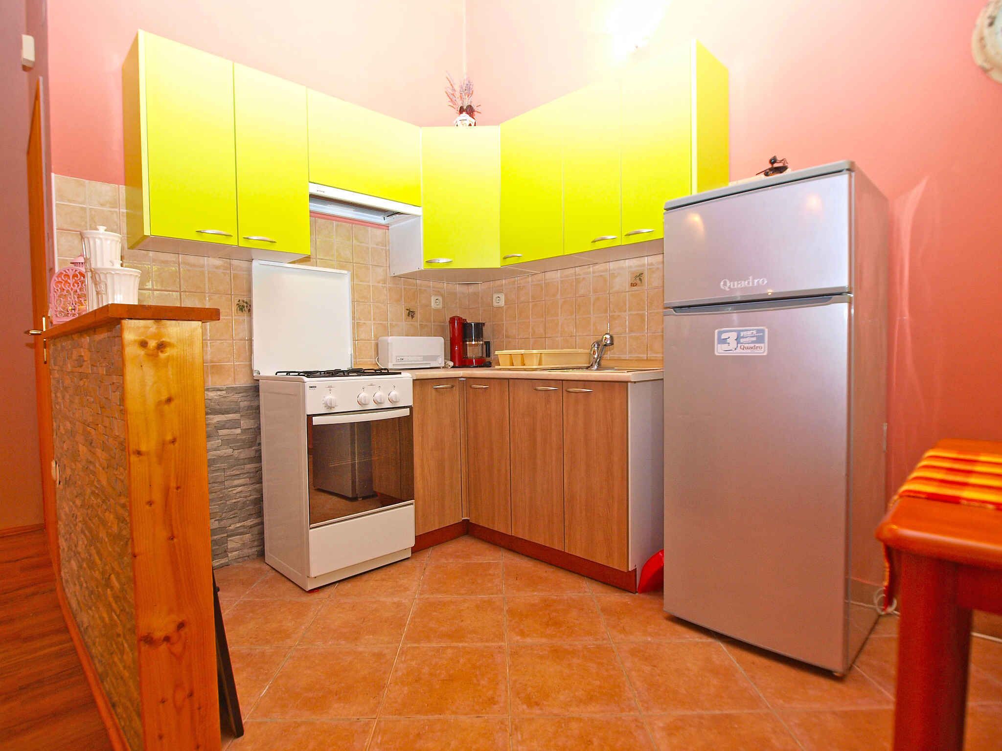 Eine kleine Küche mit Herd, Backofen und Kühlschrank, Holzschränken und Fliesenboden.