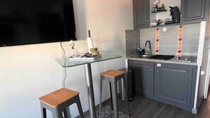 A modern kitchen with grey cabinets, a black countertop, and a glass table with two stools. - Apartment 46 (Agde)