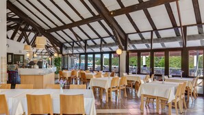 Un restaurante con mesas y sillas de madera, una zona de cocina y grandes ventanales que ofrecen vistas al exterior.