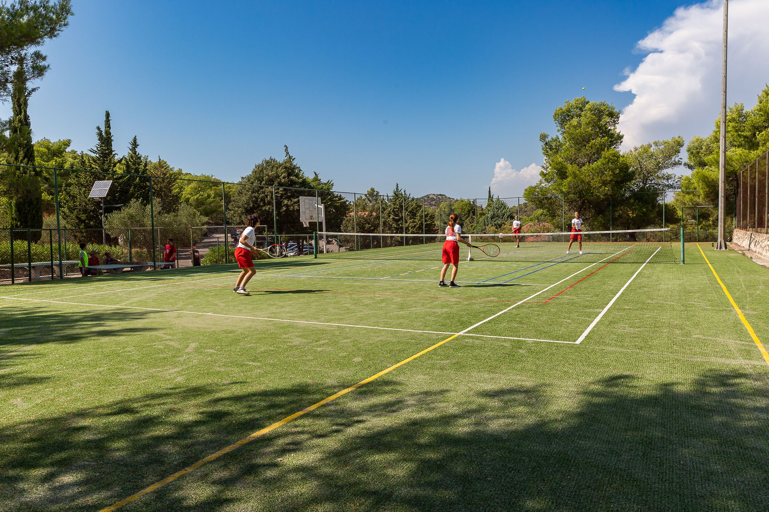A tennis court with a net, surrounded by trees and a clear sky.