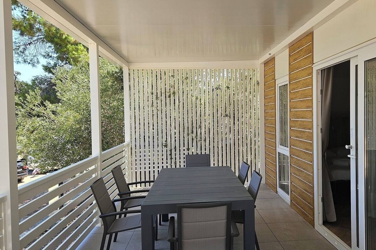 Un espace extérieur abrité, aménagé pour les repas, avec une table et des chaises, une clôture en bois et une porte-fenêtre coulissante.