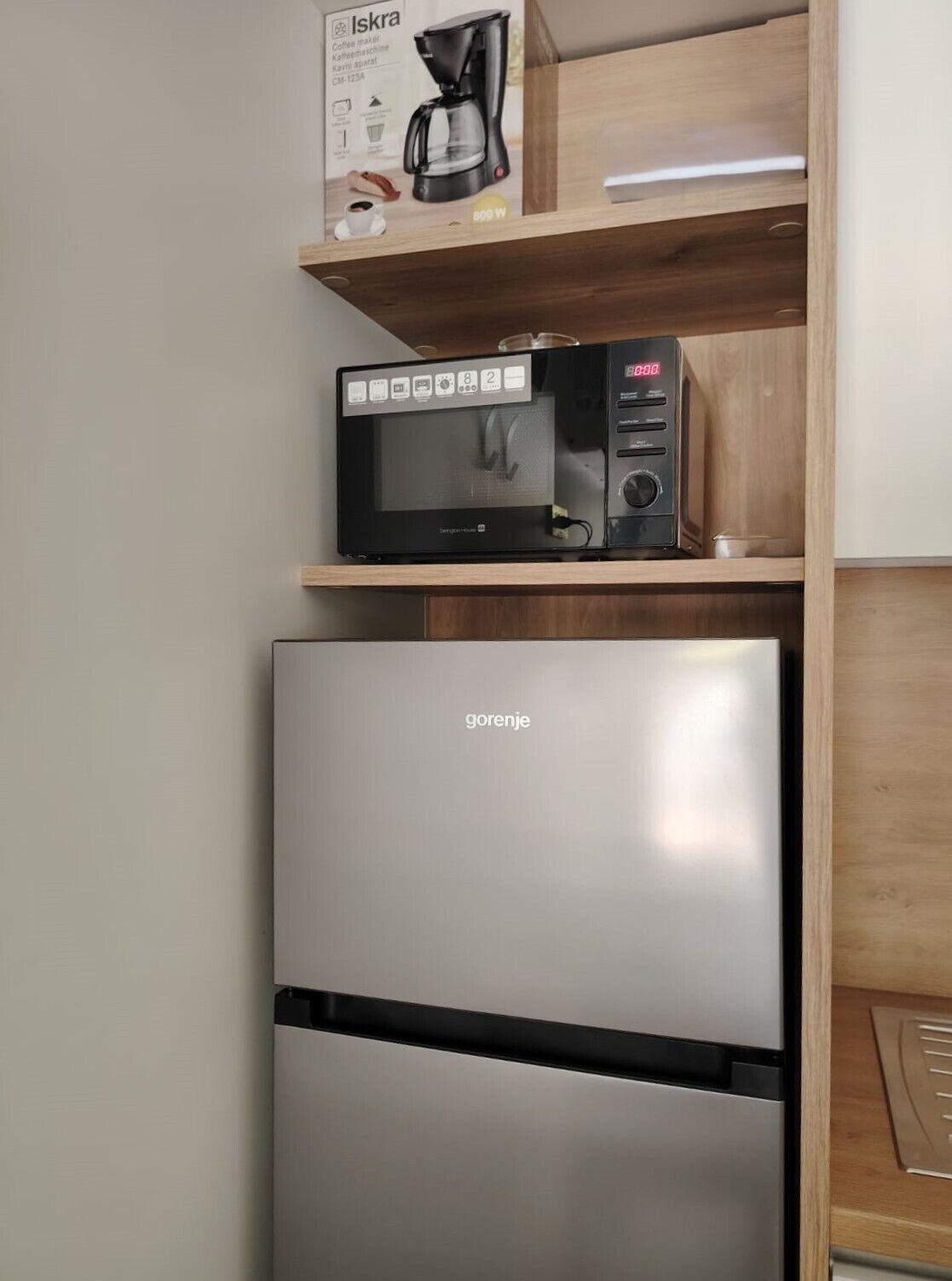 Eine Küche mit einem Edelstahl-Kühlschrank, einer Mikrowelle und einer Kaffeemaschine auf einer Holzablagefläche.