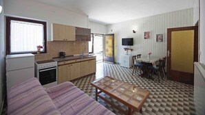 A compact kitchen with wooden cabinets, a dining table with chairs, a sofa, and a television. - Holiday apartment near the beach (Pješćana Uvala)