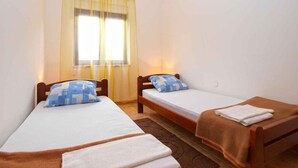 A small, clean room with two single beds, a window with yellow curtains, and a brown rug.