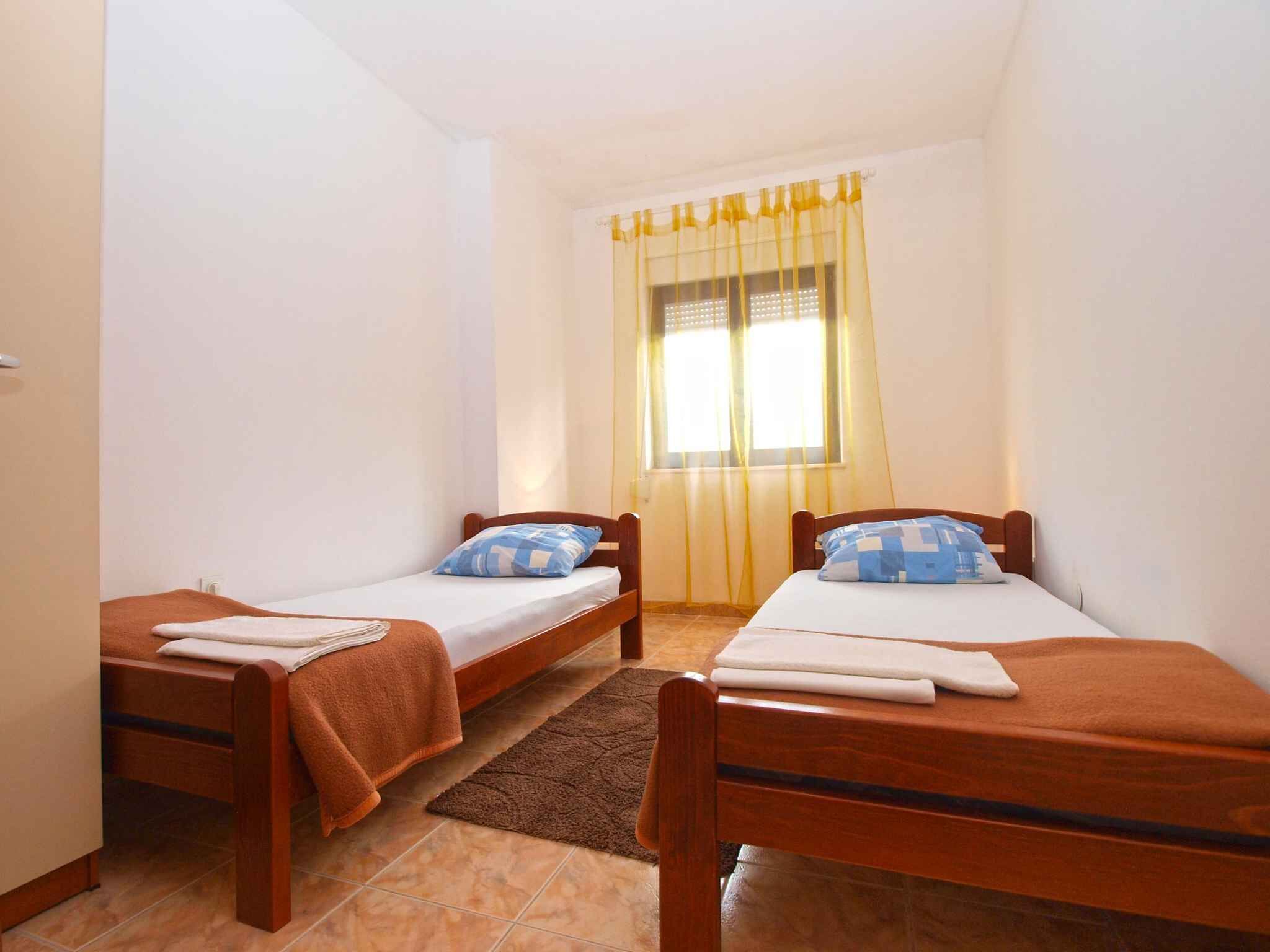 Une petite chambre propre, avec deux lits simples, une fenêtre ornée de rideaux jaunes et un tapis marron.