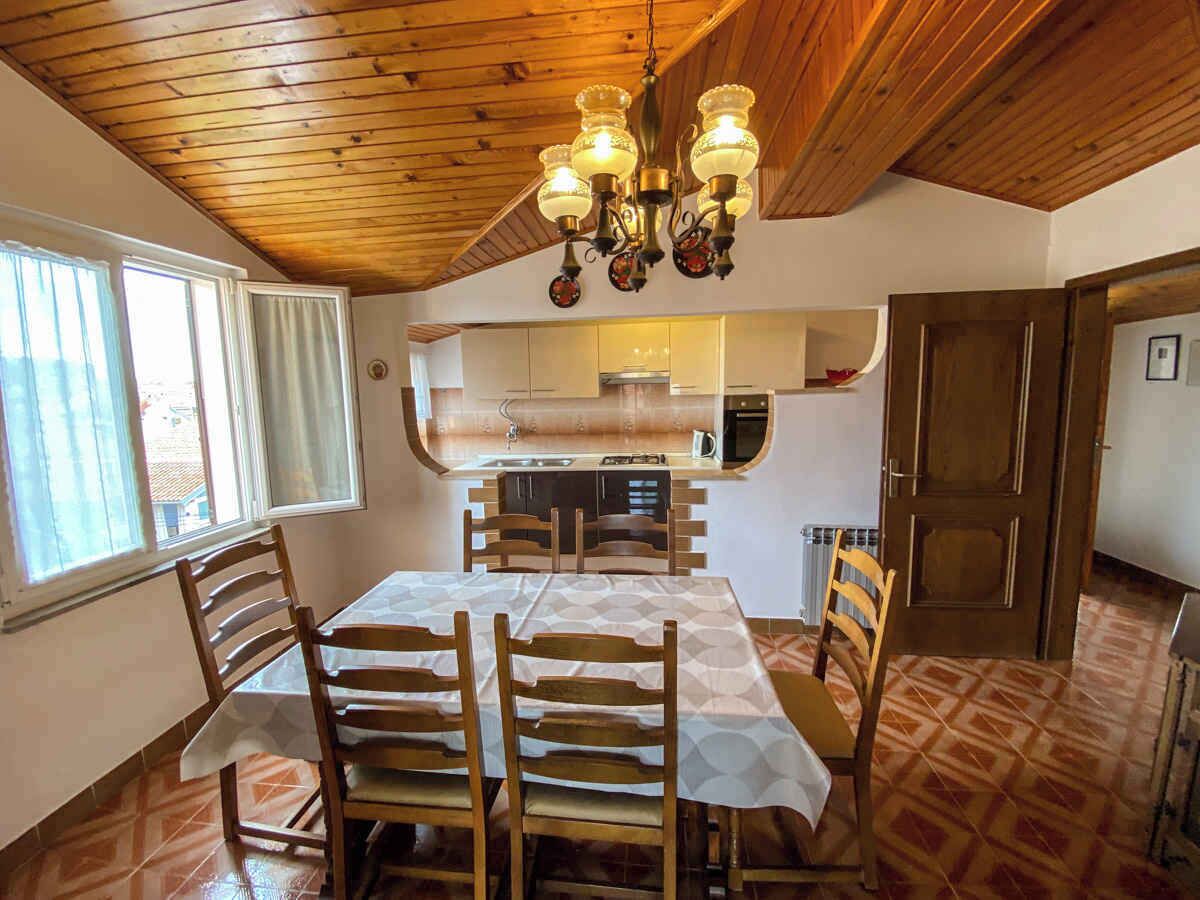 Un comedor con techo de madera, una araña y una cocina al fondo.