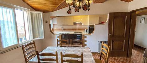Un comedor con techo de madera, una araña y una cocina al fondo.