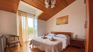 Une chambre à coucher avec un plafond en bois, un lit recouvert d’une couvre-lit à motifs, une table de chevet, une chaise et une fenêtre avec des rideaux.