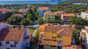 Une ville côtière aux bâtiments aux toits de tuiles rouges, offrant une vue dégagée sur la mer et entourée d’une végétation luxuriante.