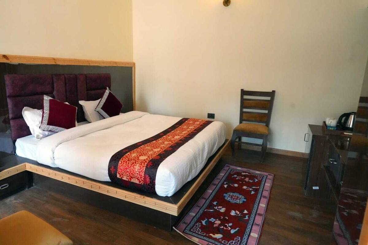 A bedroom with a bed, a wooden nightstand, a chair, and a desk with a kettle.