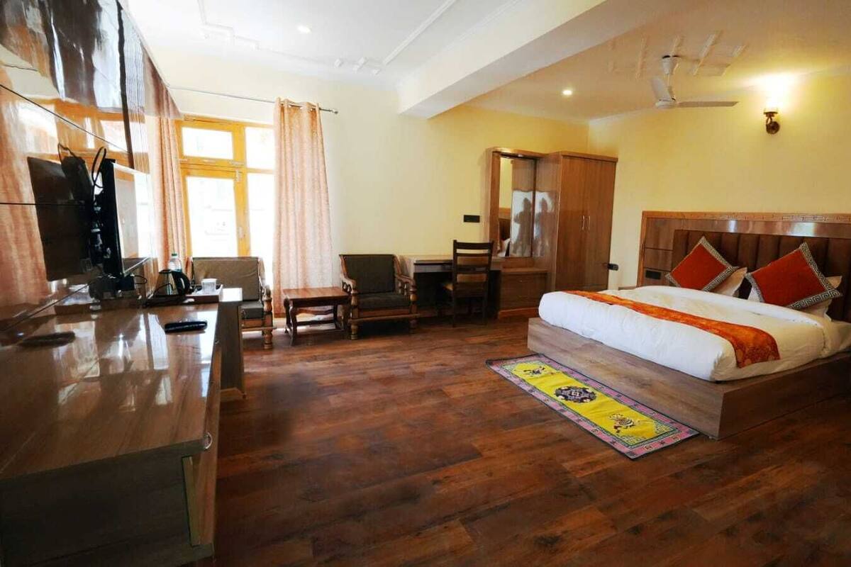 A hotel room with a wooden floor, a bed with a headboard, a desk, a chair, and a wardrobe.