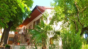 Ein Gebäude mit rotem Dach, Steintreppe und einem Garten mit verschiedenen Pflanzen und einer Palme.