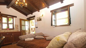 A bedroom with a large bed, wooden ceiling beams, a window with a view, a small desk, and a chair.