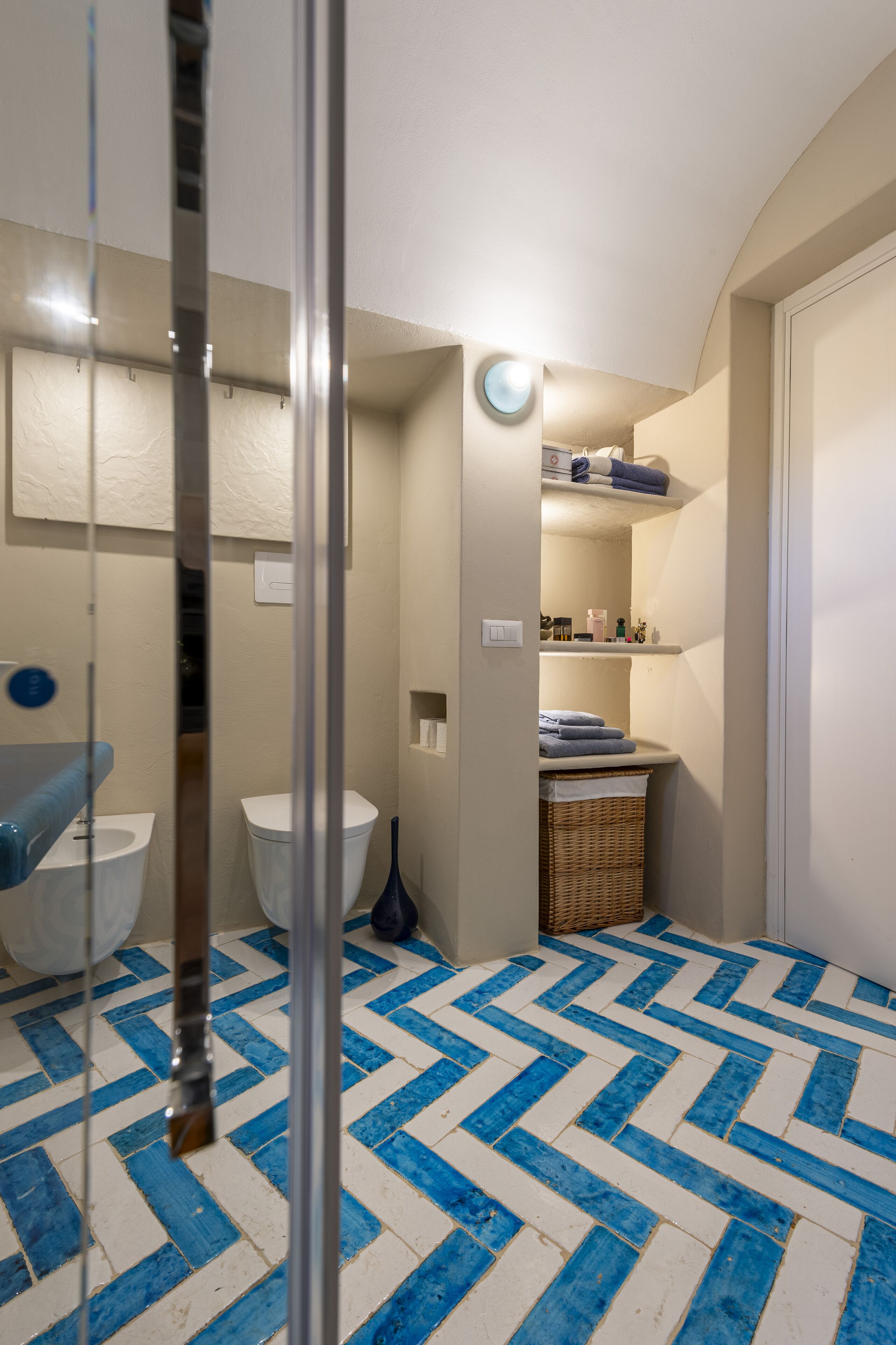A bathroom with a blue and white herringbone floor pattern, a white toilet, a blue sink, and a wicker basket on the floor.