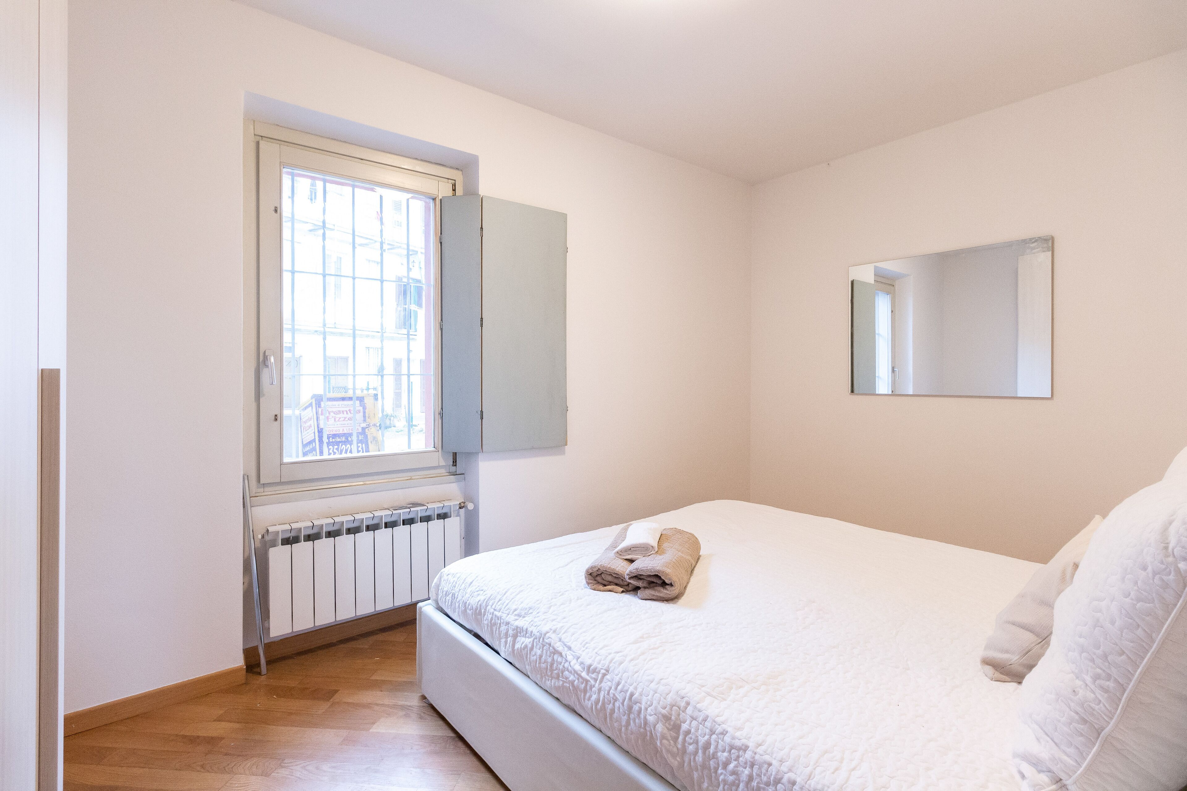 Une chambre à coucher avec un lit, une fenêtre, un radiateur et un miroir au mur.