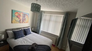 A bedroom with a bed, a painting, a window with blinds, and a hanging light fixture.