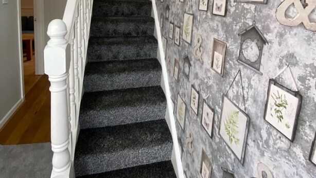A staircase with a patterned wallpaper and framed pictures on the wall.