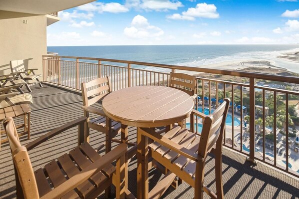 A balcony with wooden furniture, a round table, and a view of the beach and ocean.