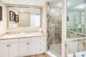 A bathroom with a large mirror, two sinks, a shower enclosure, and a bathtub.