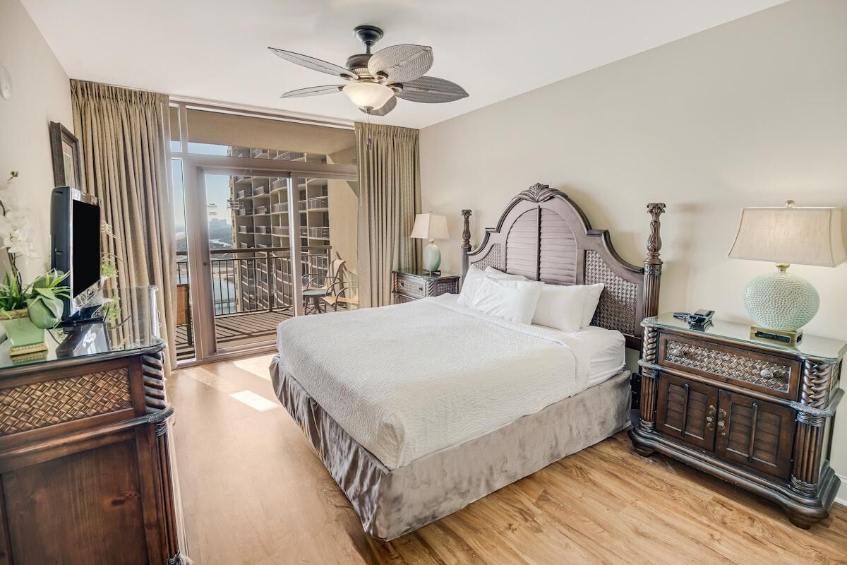 Une chambre d’hôtel avec un grand lit, un ventilateur de plafond, une table de chevet, une lampe et une vue sur l’extérieur.