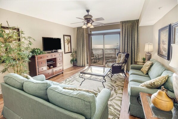 A living room with a sofa, a coffee table, a TV, and a balcony with a view.