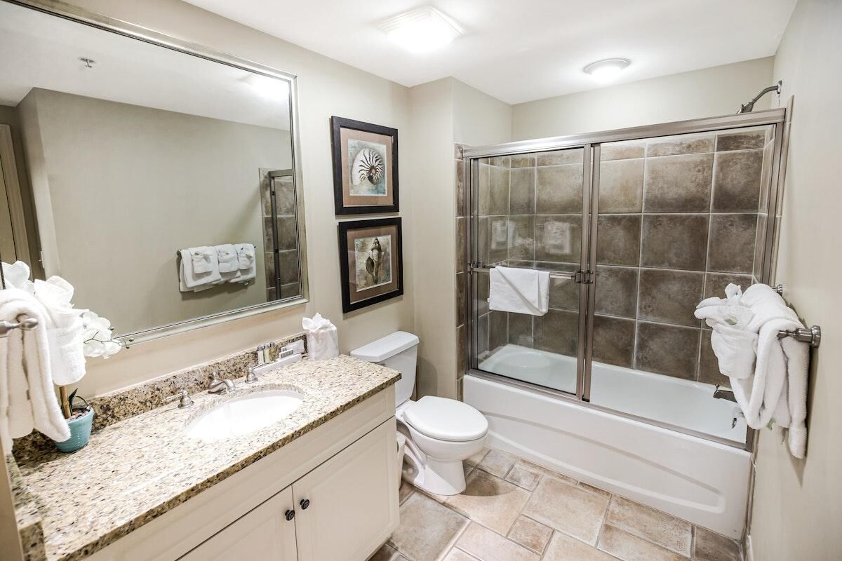 Un baño con lavamanos de encimera de granito, inodoro, bañera y ducha con mampara de vidrio.