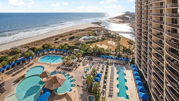 Ein Resort mit mehreren Schwimmbecken, einem Strand und einem Hochhaus.