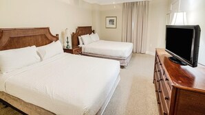 Une chambre d’hôtel avec deux lits, un ventilateur de plafond, une télévision et une commode.